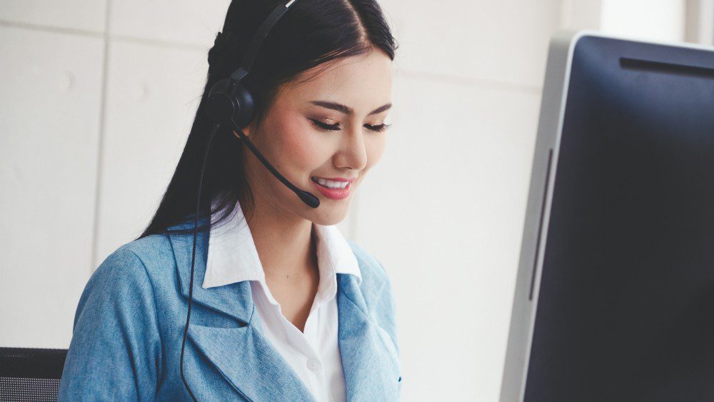 Smiling woman wearing a headset working on a computer.