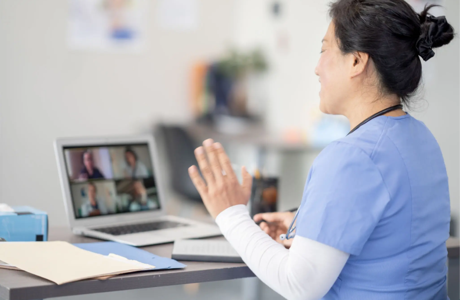 A nurse video calling patients, waving from her desk.